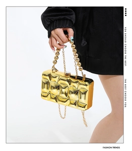 Detail of gold metallic hard shell evening clutch with quilted texture and bead handle