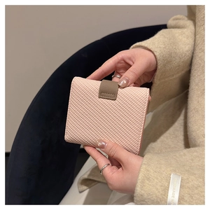 Close-up of a woven texture pink wallet with a dark brown leather clasp held by a model