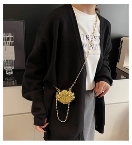 Detail of a shiny gold shell mini bag with a beaded chain on a model wearing black