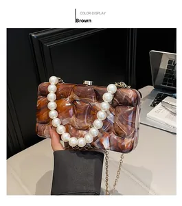 Detail of brown marble acrylic clutch with white pearl handle and gold chain strap