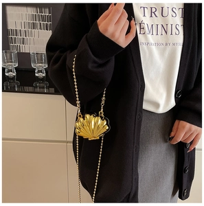 Detail of a golden metallic shell-shaped crossbody bag with a fine bead chain strap