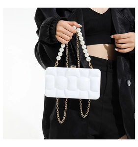 Detail of white acrylic clutch with pearl handle and golden chain over black dress