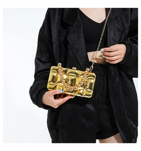Detail of a gold metallic clutch with quilted texture and beaded handle on a black outfit