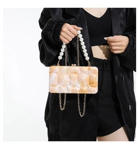 Detail of acrylic evening clutch with marble texture, pearl handle and gold chain strap