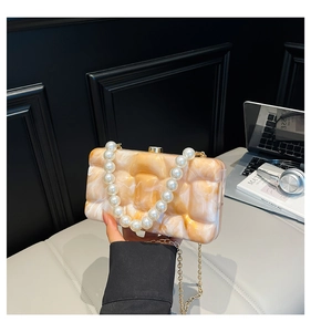 Detail of orange marble amber acrylic evening clutch with pearl handle and gold chain