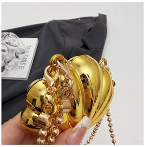 Macro detail of glossy golden shell-shaped evening bag with ribbed metal texture and chain