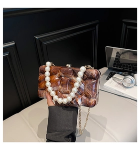 Detail of amber marble acrylic evening clutch with large pearl handle and gold chain strap