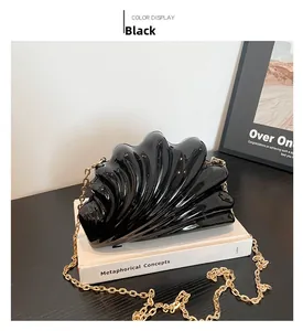 Glossy black shell-shaped acrylic clutch with wavy texture and gold chain on white books