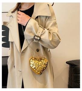 Detail of a heart-shaped gold evening bag with textured metallic surface on a trench coat