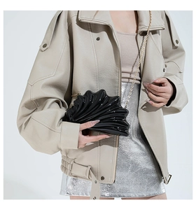 Black acrylic shell clutch bag with gold chain strap shown on a model in detail