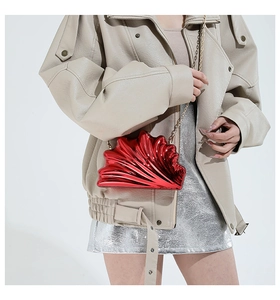 Macro view of red shell-shaped evening bag featuring metallic gloss and gold chain strap