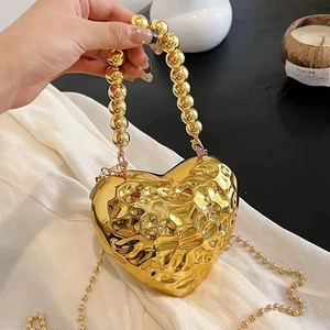 Detailed view of heart-shaped gold clutch featuring a textured surface and beaded handle