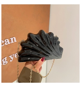 Detail of a shiny black shell-shaped acrylic clutch with fine gold chain strap