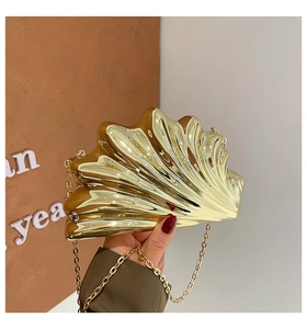 Detail of golden shell-shaped evening clutch with polished texture and metal chain