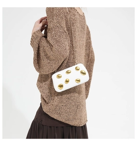 Close-up of white clutch bag with gold metallic pebble accents and delicate chain strap