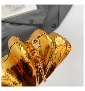 Macro view of gold shell evening bag featuring a metallic mirror finish and chain strap