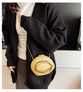 Detail of a bright yellow crossbody bag with a large gold metal ring and chain strap