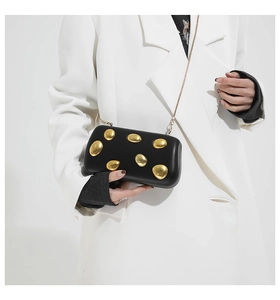 Detail of a black structured evening bag featuring gold pebble metal accents and chain strap