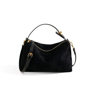 Detail of black quilted suede handbag with gold zipper and adjustable shoulder strap