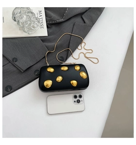 Detail of black PU evening clutch with gold pebble accents and chain strap next to a phone