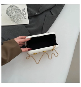Detailed view of white hard-shell evening clutch with gold spherical accents and black lining
