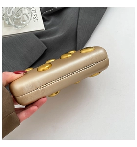 Detail of champagne gold minaudiere bag with oval metal studs and textured leather finish