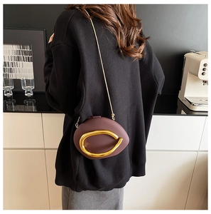 Close-up of deep purple pebble-shaped crossbody bag with gold ring handle and chain strap