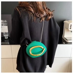Detail of green round clutch bag with large gold C-clasp and metal chain strap on model