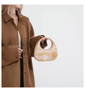 Chic amber resin crescent handbag shown styled with a brown suede coat on a model