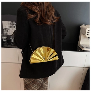 Golden fan-shaped evening clutch bag with chain strap worn by model in a modern room