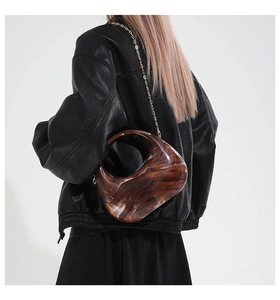 Detail of a brown marble acrylic handbag featuring a sleek gold chain and crescent shape