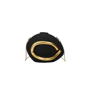 Detail of matte black evening bag with a large C-shaped gold metal buckle and chain strap