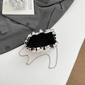 Silver wavy acrylic evening bag with shell shape and metal chain strap on white desk