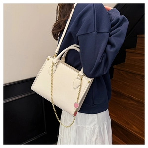 Détail du sac à bandoulière blanc crème avec texture litchi, chaîne dorée et breloque fraise