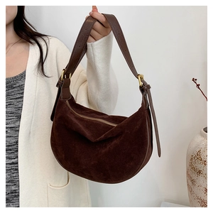 Close-up of a dark brown suede crescent bag with leather straps and golden metal hardware
