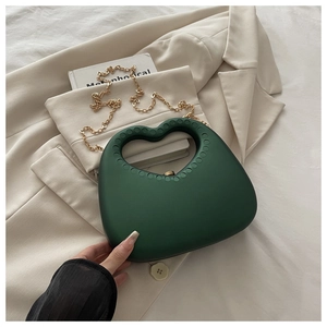Detail van donkergroene hartvormige avondtas met gouden ketting op een blazer