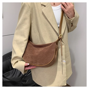 Detail of brown suede crescent bag showing matte texture and gold buckle on a model