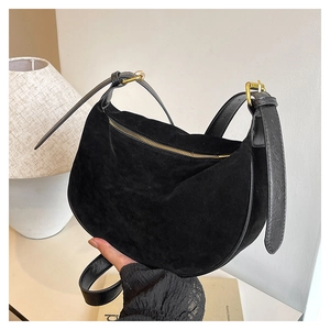 Close-up of black suede crescent bag with smooth leather strap and gold zipper detail