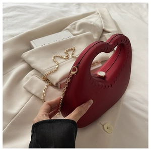 Detail van rode hartvormige clutch tas met gouden ketting en een elegante ringgreep