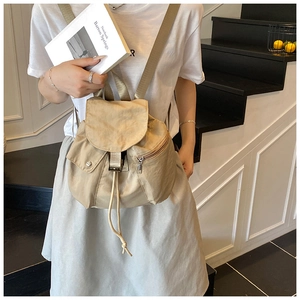 Detail of minimalist beige drawstring backpack with side zipper on indoor stairs