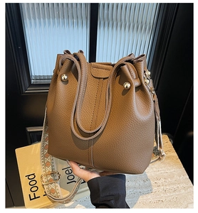 Close-up of brown pebbled leather bucket bag with a colorful woven wide strap
