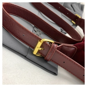 Close-up of deep red leather belt with polished gold square buckle on gray pleated fabric