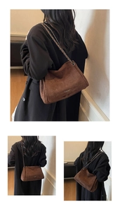 Detail of dark brown suede shoulder bag with metal chain strap and minimalist gold logo