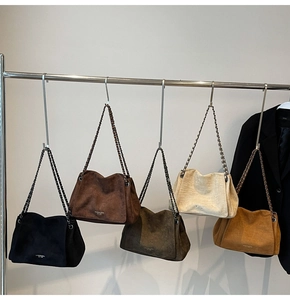 Five suede shoulder bags with chain straps in multiple colors hanging on a metal rack