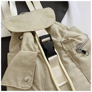 Detailed close-up of beige nylon backpack featuring black buckle and silver zipper