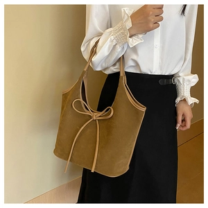 Brown suede shoulder bag with bow detail held by model against a warm beige background