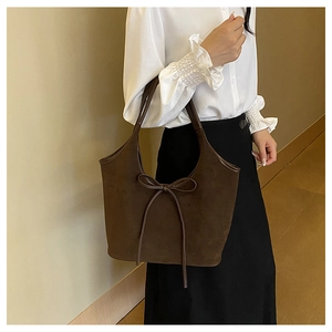 Detail of dark brown suede tote bag featuring a decorative bow and dual shoulder straps