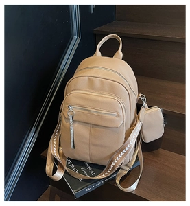 Detail of khaki pebbled leather backpack featuring wide woven strap and mini pouch charm