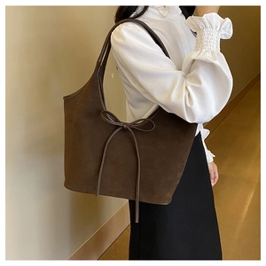 Detail of a dark brown suede tote bag featuring a decorative soft bow and shoulder strap