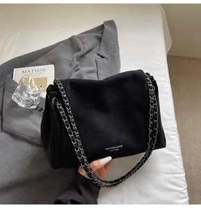 Close-up of black suede shoulder bag with silver chain strap and brand logo